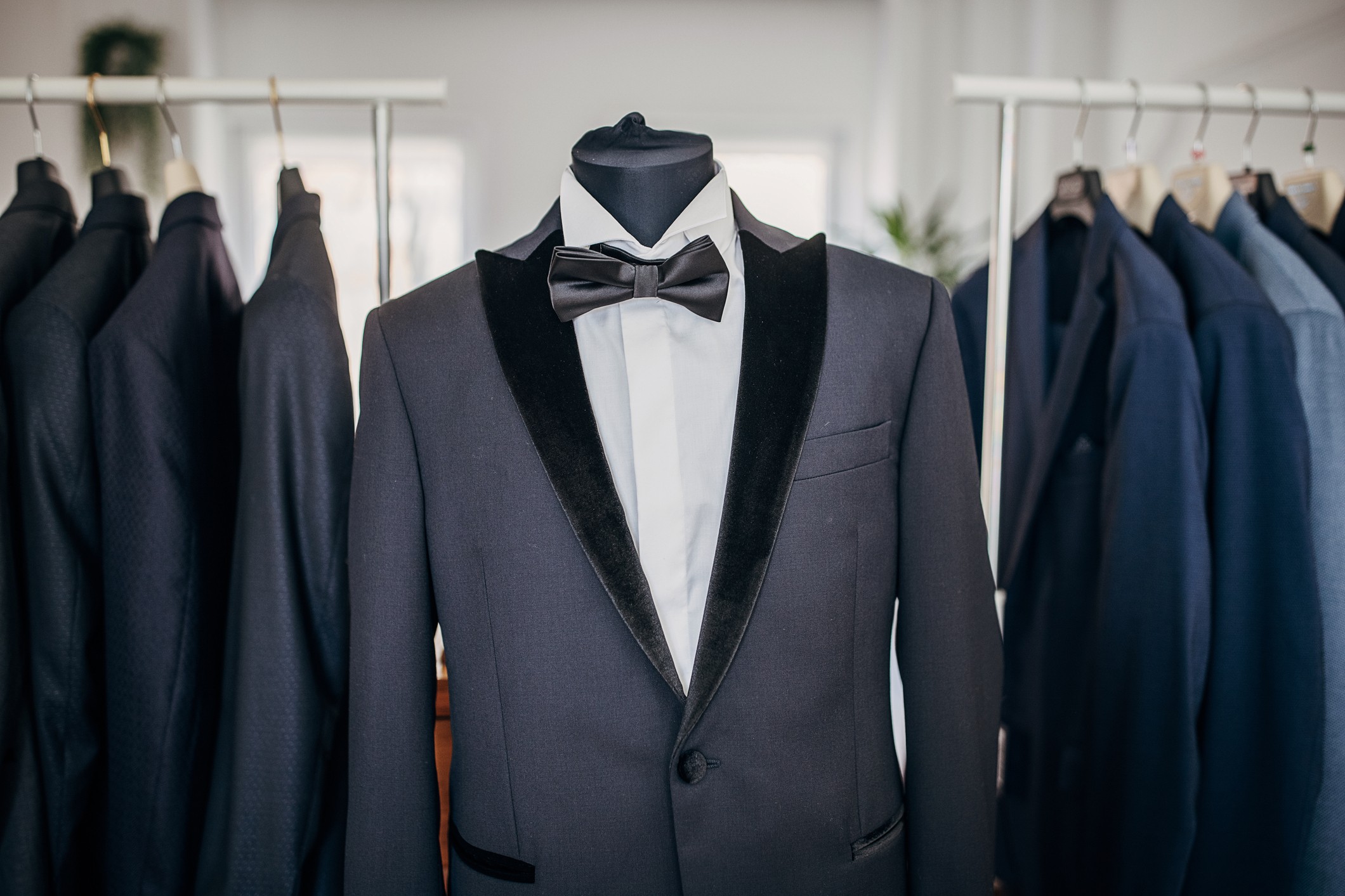 Tuxedo displayed among suits on rack.