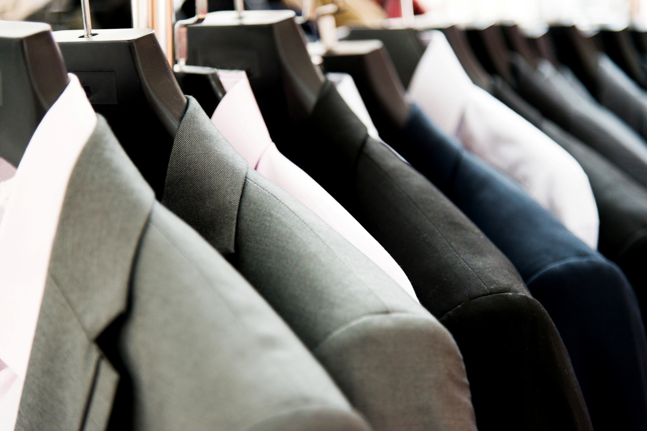 Men's suits hanging on a clothing rack.