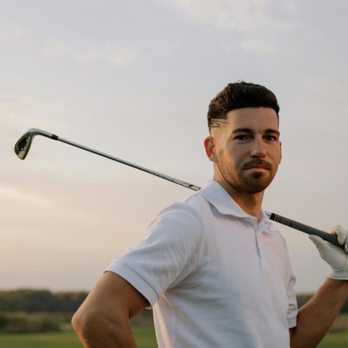 Golfer holding golf club over shoulder at sunset